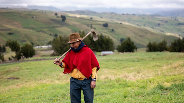 A man walks through a field with a hoe