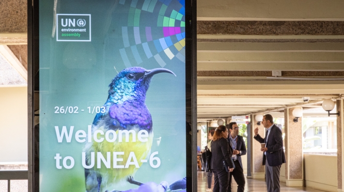 UN Environment Assembly delegates in discussion beside a digital screen that welcomes participants to the sixth session at the United Nations Office in Nairobi 