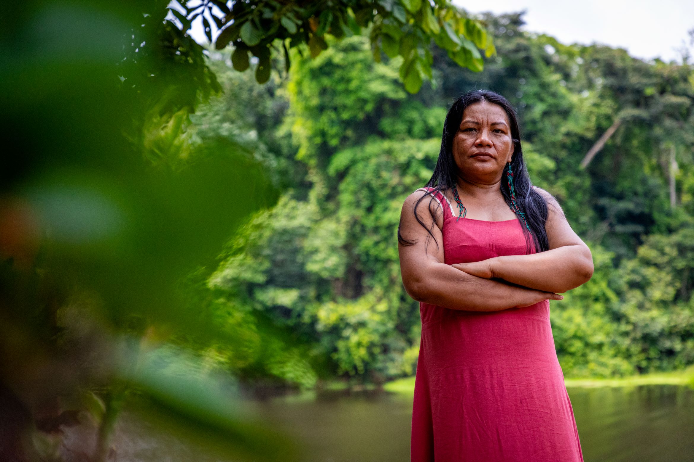 A woman stands with her arms crossed, a river and dense foliage behind her 