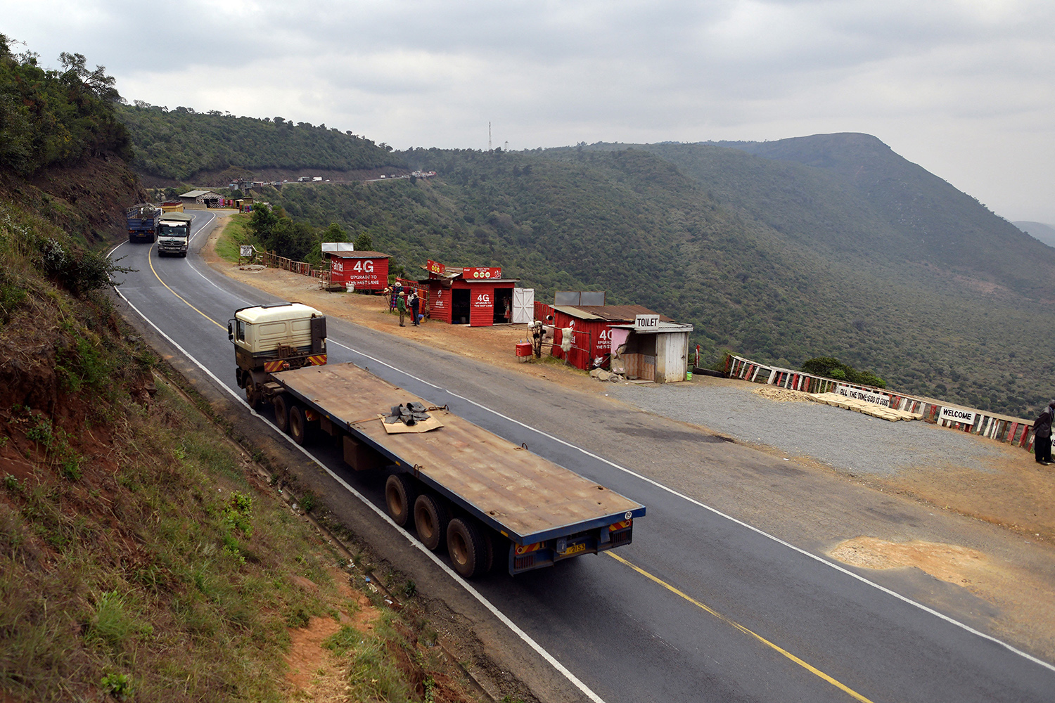 Trucks rumble along a road overlooking a deep valley