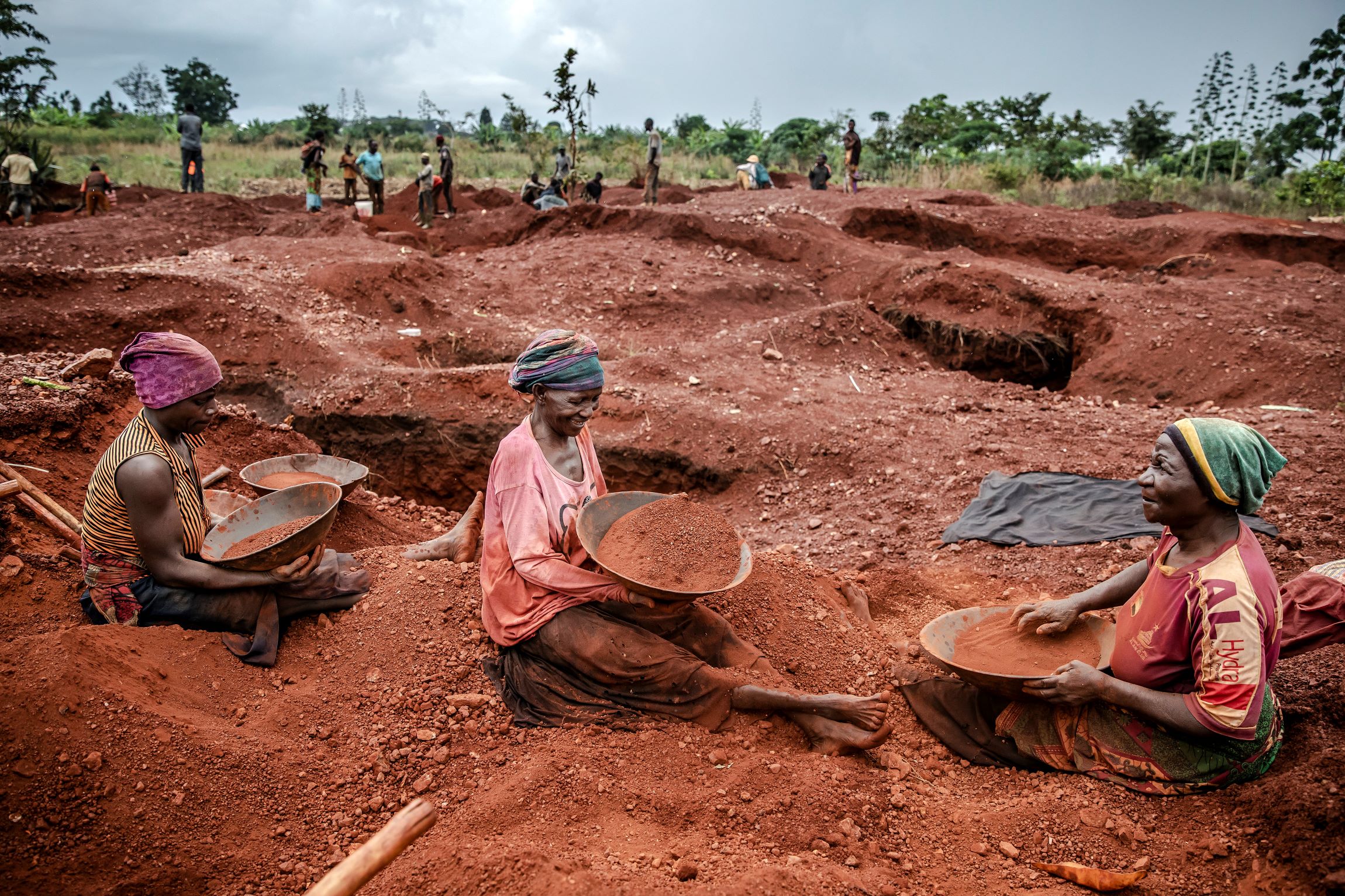  Three women sitting in red dirt, panning for gold and chatting. 