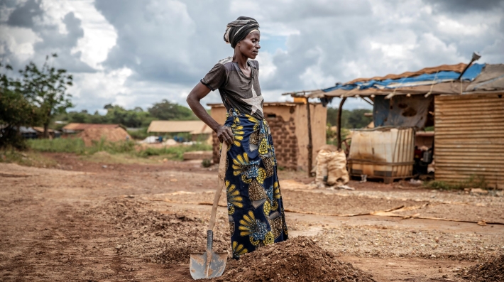 A woman standing in a pit holding a shovel, a hand on her waist. 