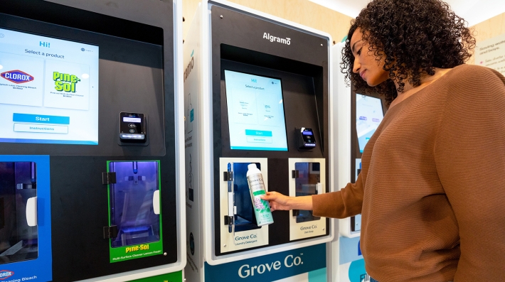 A woman brings a small reusable can to a refill machine for laundry detergent.